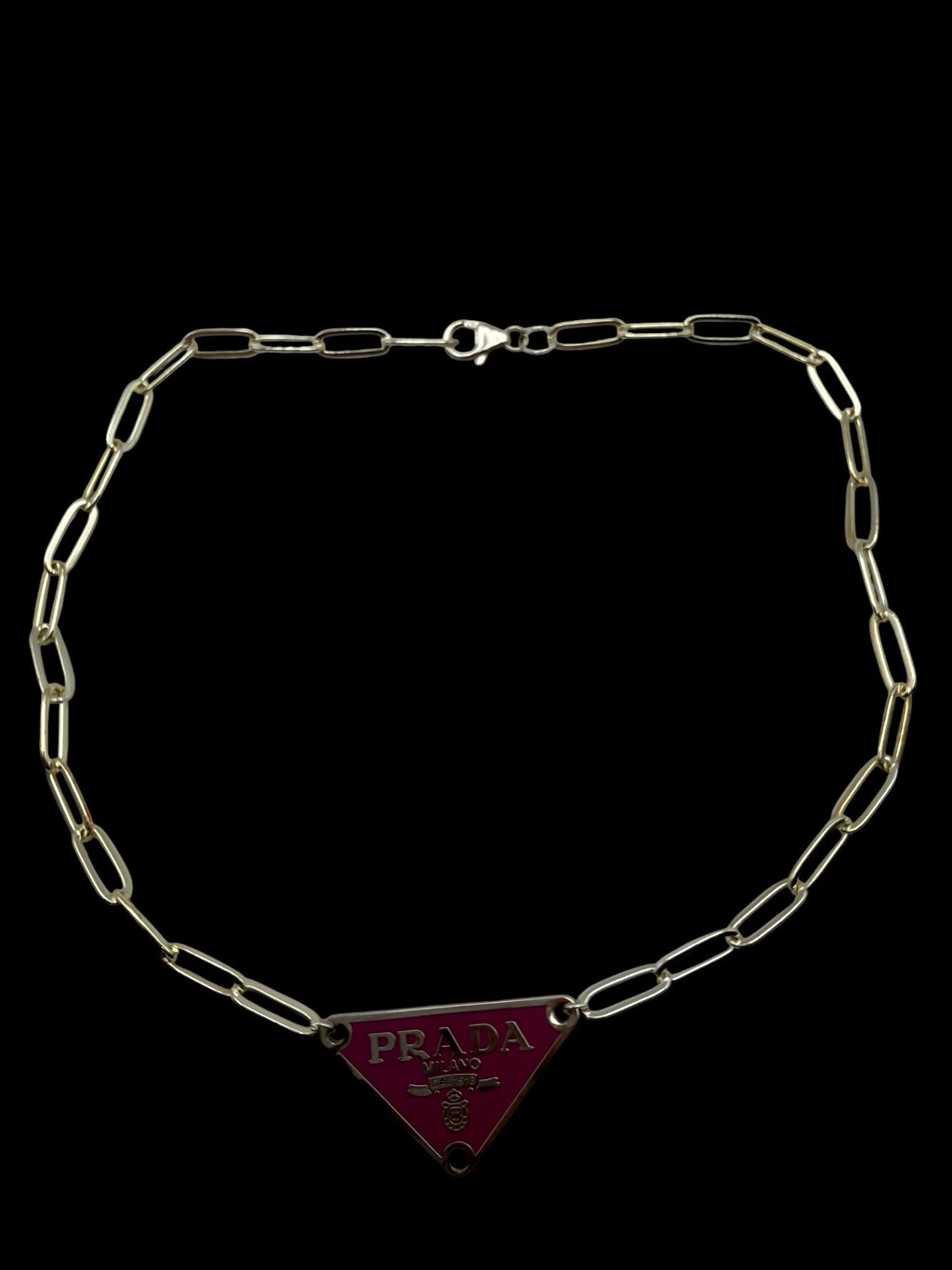 Silver chain necklace with a Prada triangle logo pendant on a black background