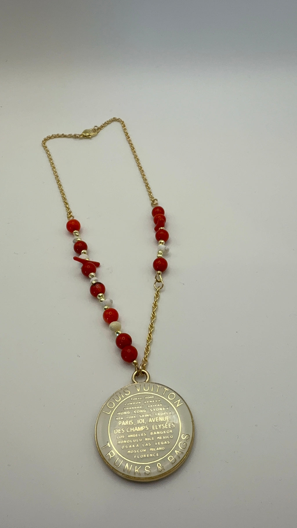 Necklace with red beads and a gold pendant on a light gray background