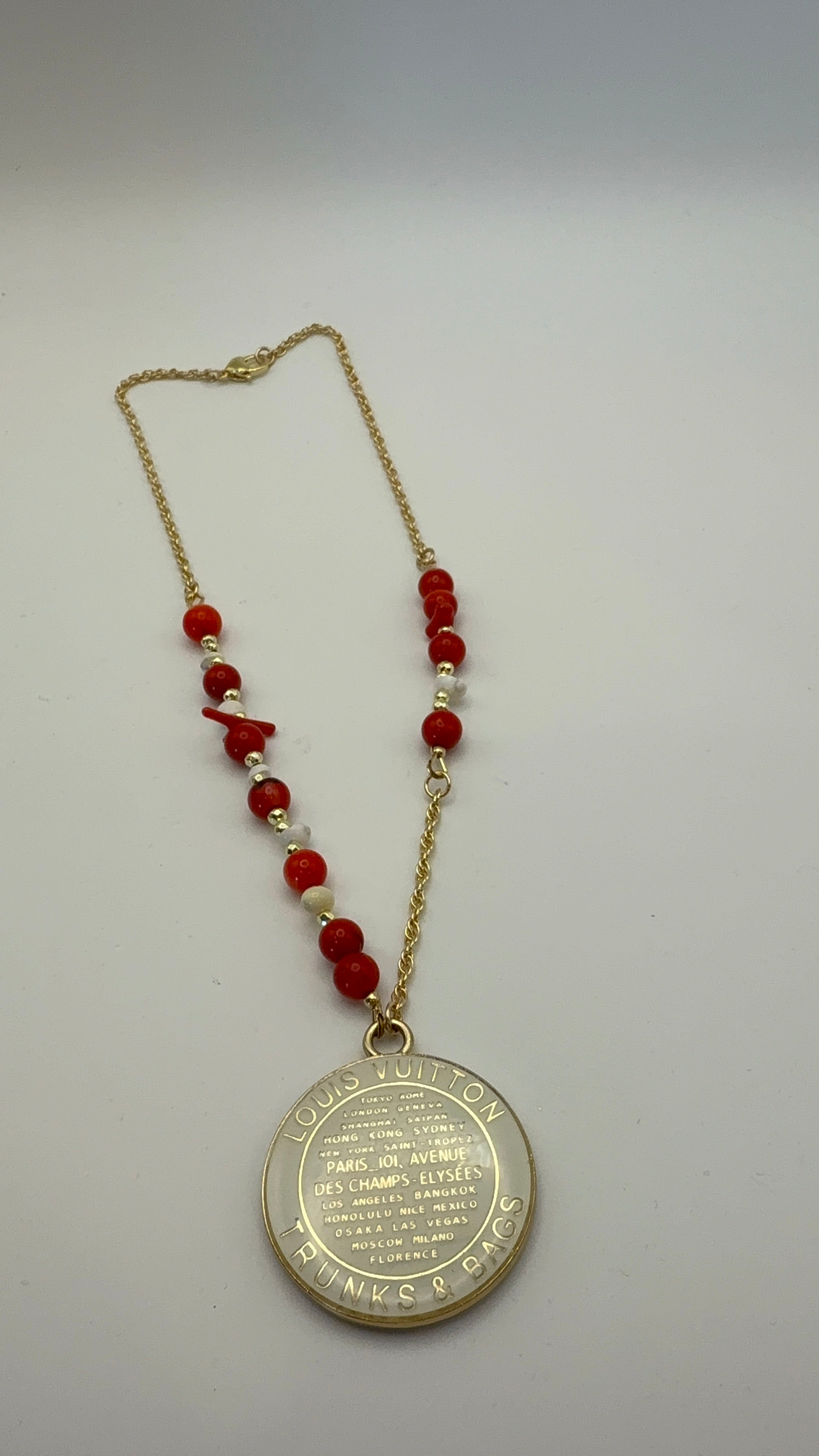 Necklace with red beads and a gold pendant on a light gray background