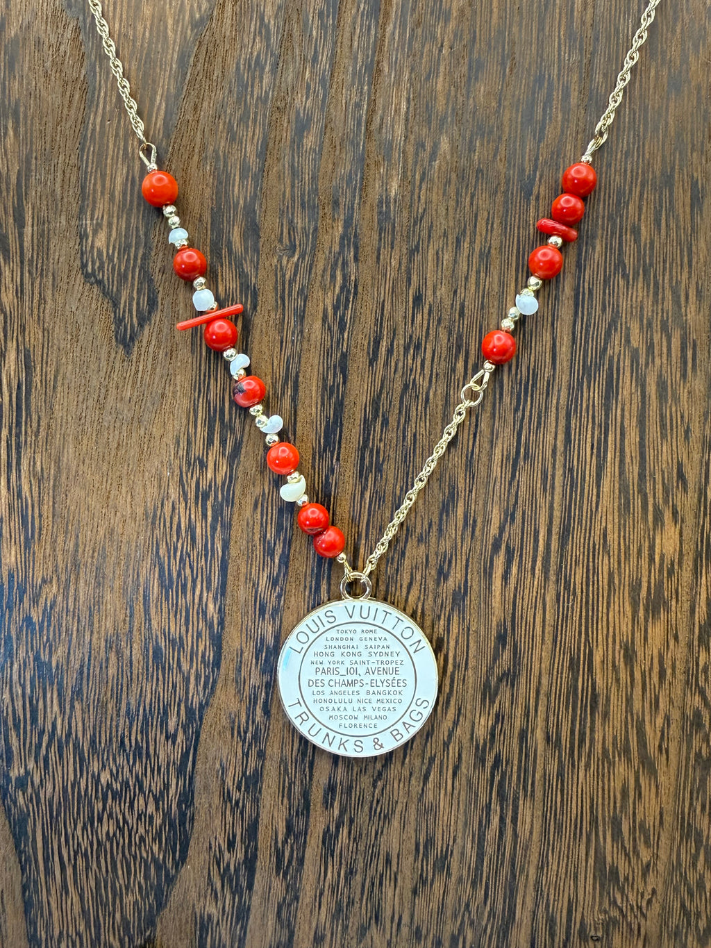 Necklace with red and white beads and a silver pendant on a wooden surface