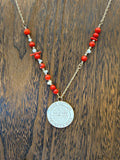 Necklace with red and white beads and a silver pendant on a wooden surface