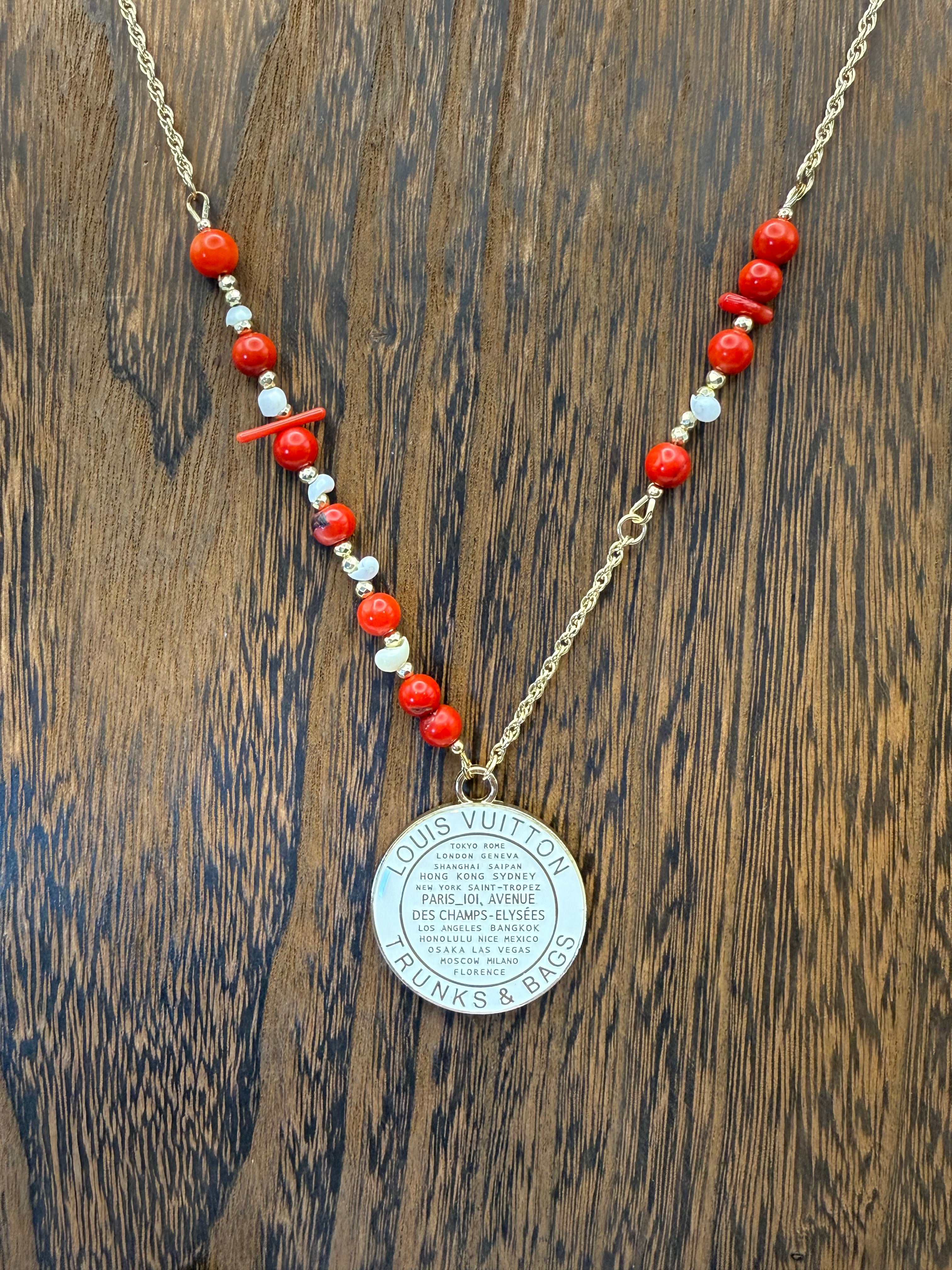 Necklace with red and white beads and a silver pendant on a wooden surface