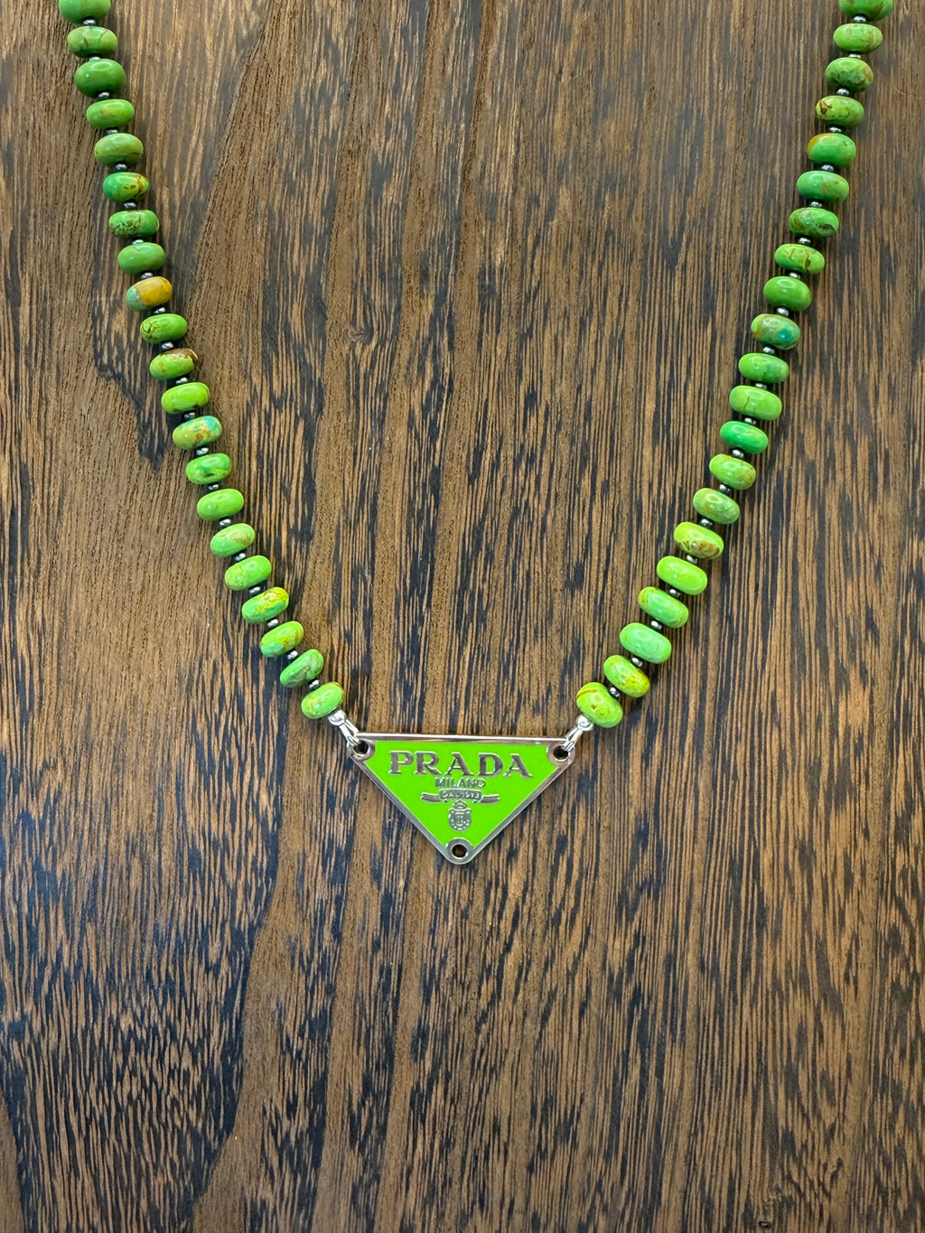Green beaded necklace with Prada triangle logo on a wooden surface
