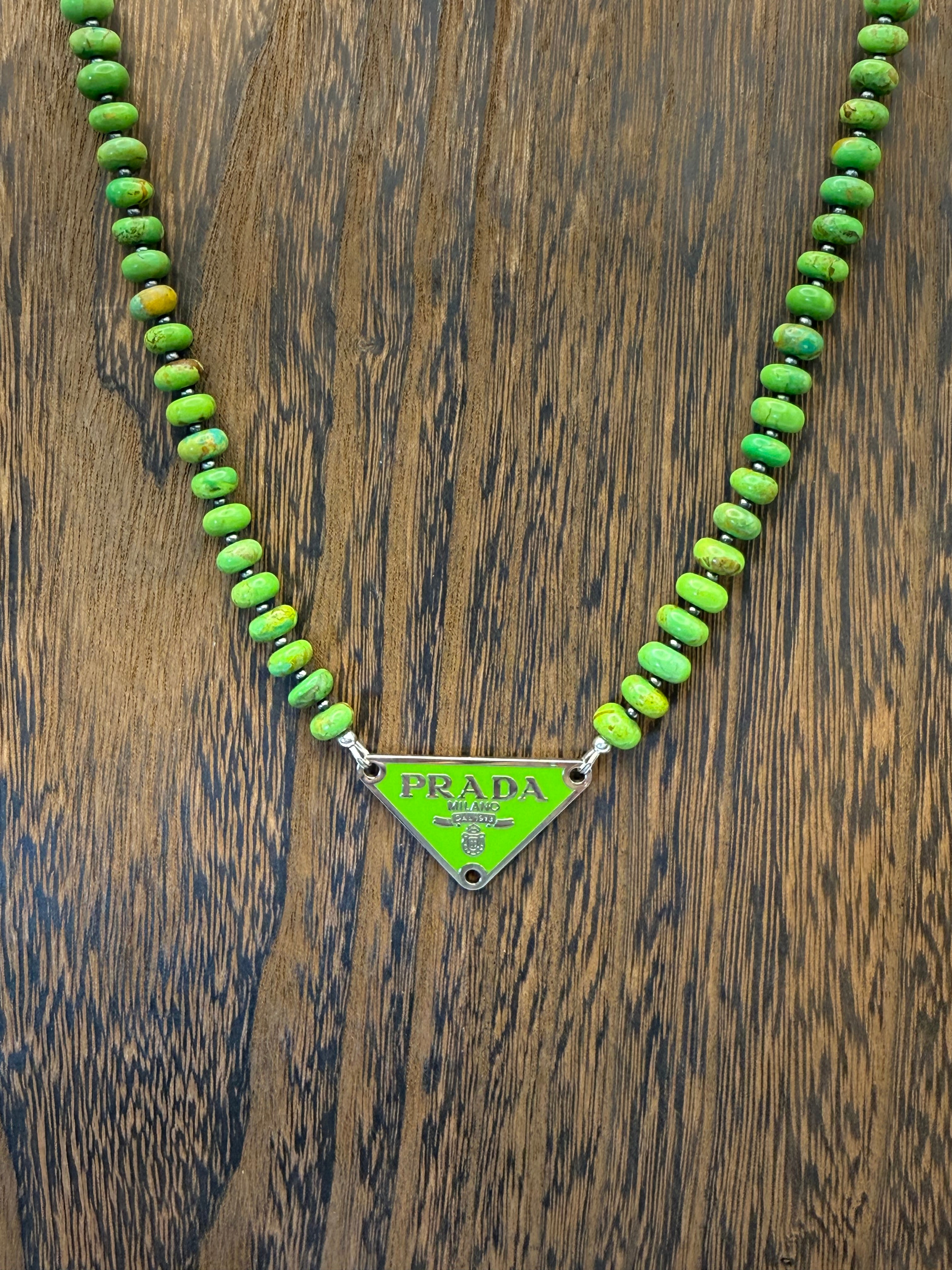 Green beaded necklace with Prada triangle logo on a wooden surface