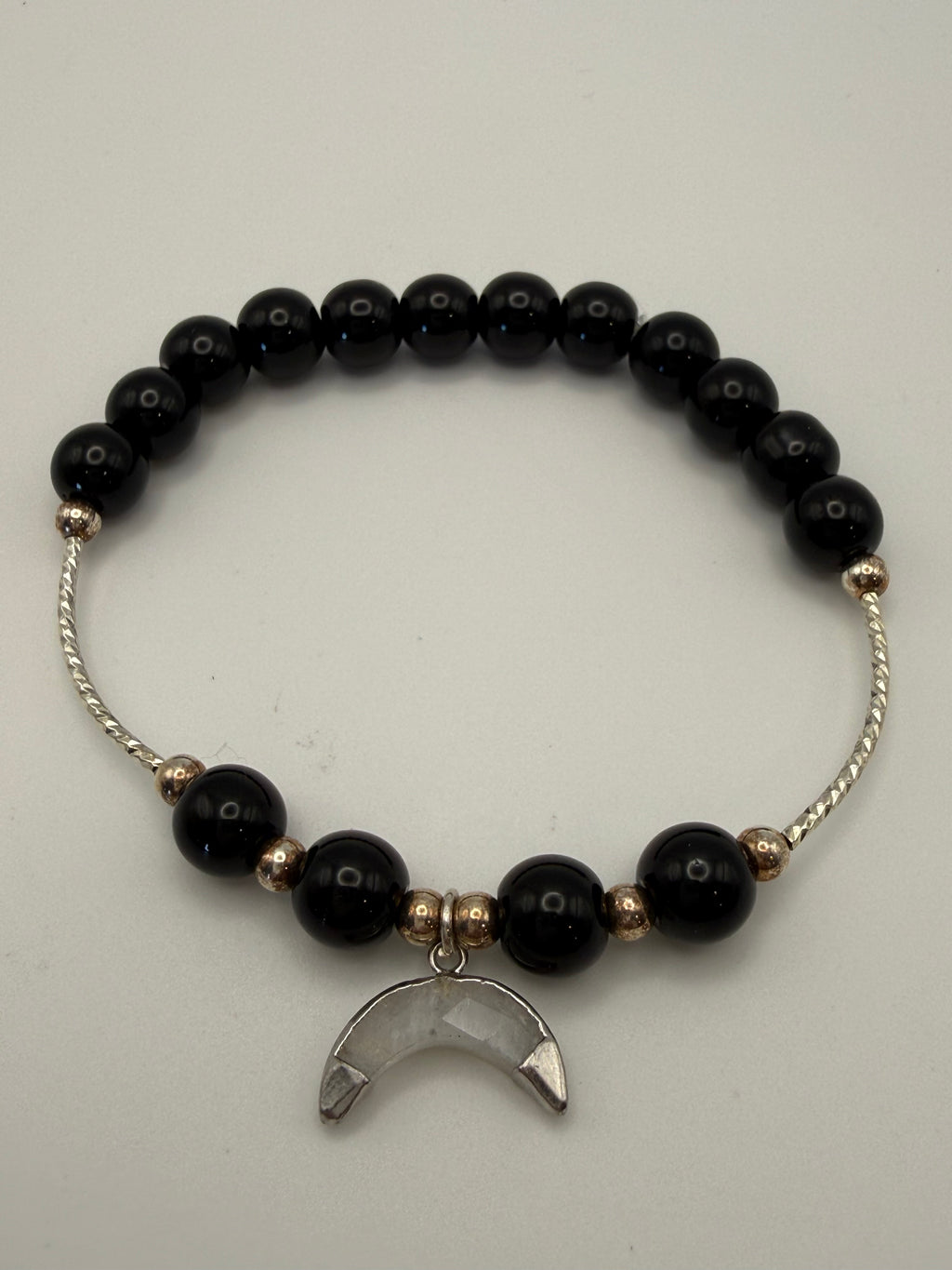 Black beaded bracelet with a silver moon charm on a light gray background