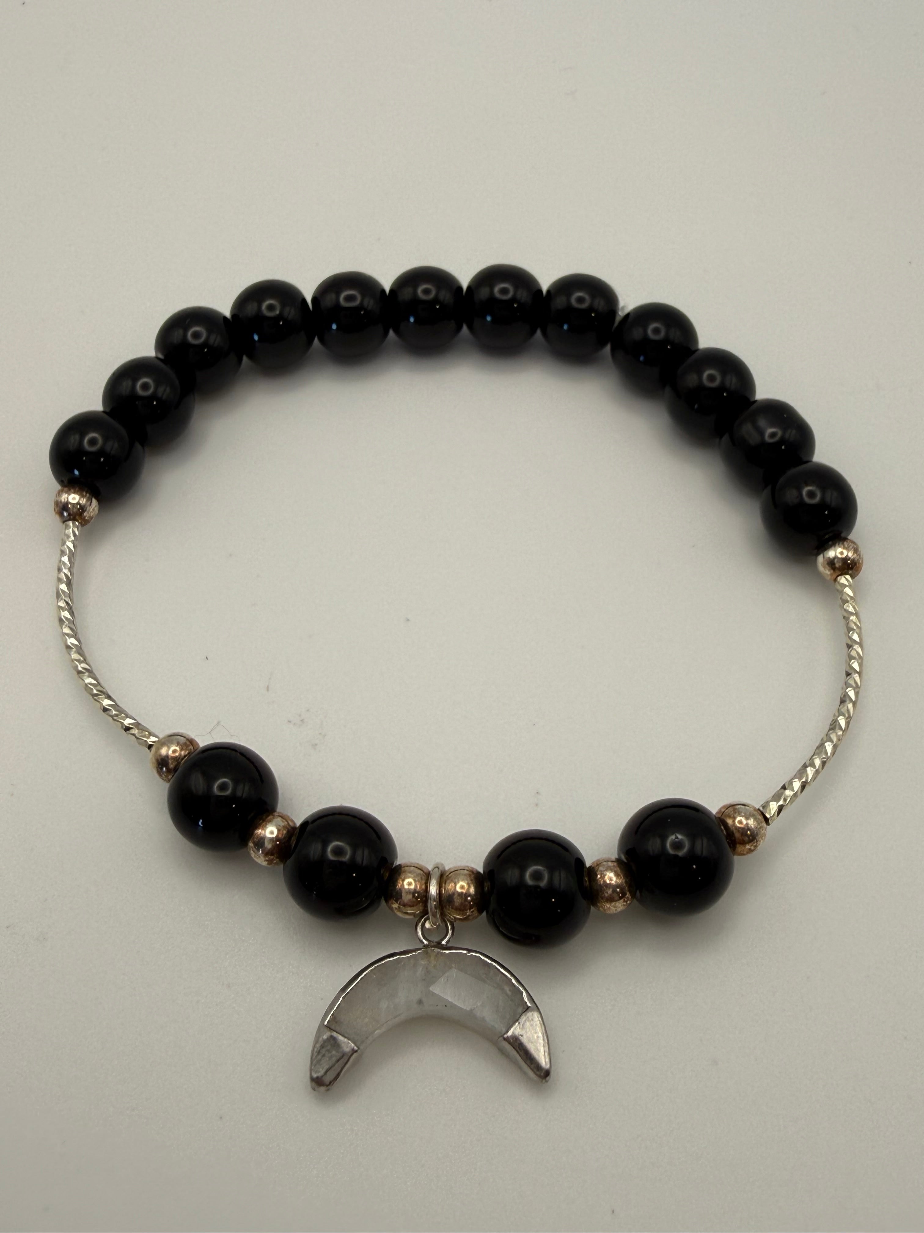 Black beaded bracelet with a silver moon charm on a light gray background