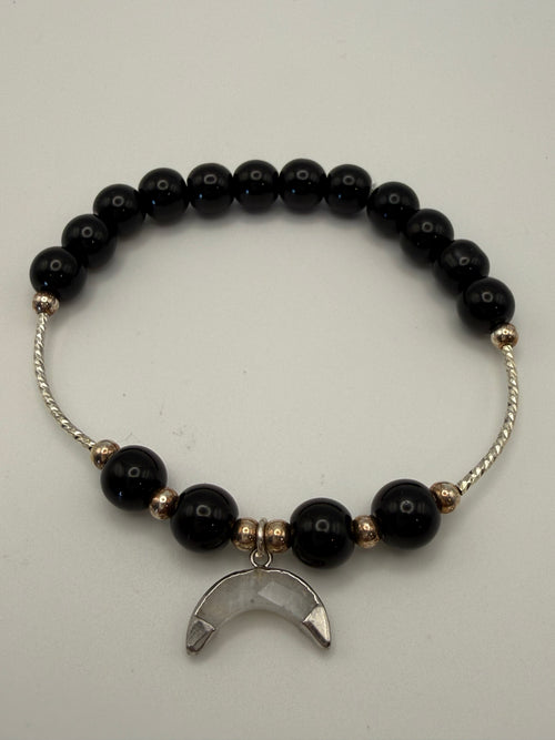 Black beaded bracelet with a silver moon charm on a light gray background