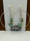 Silver earrings with turquoise stones on a white card with black floral design