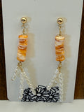Beaded earring with orange and gold beads on a white card with black floral design