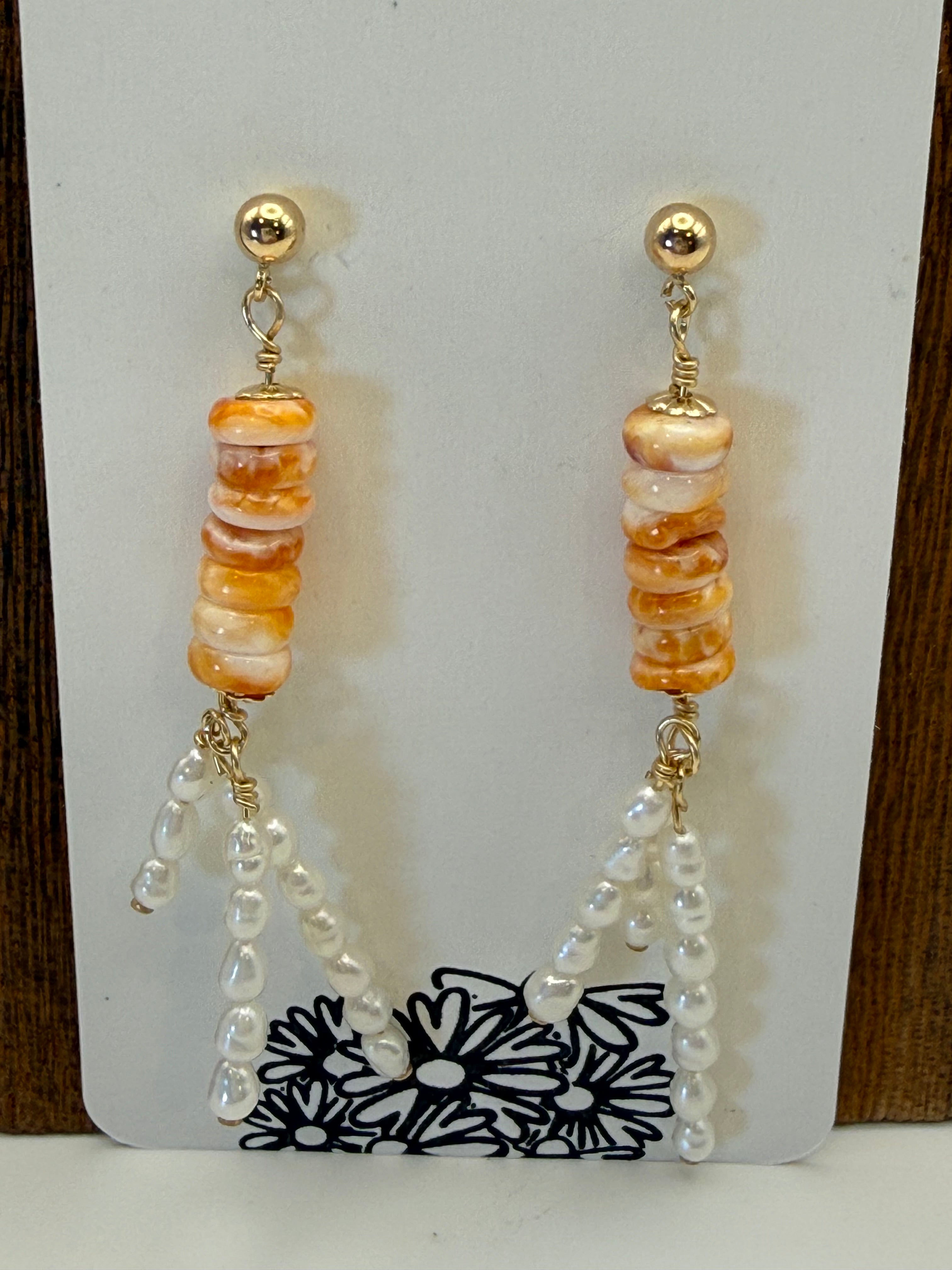 Beaded earring with orange and gold beads on a white card with black floral design