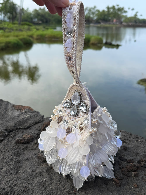 Decorative handbag with floral and gemstone details held against a natural background.