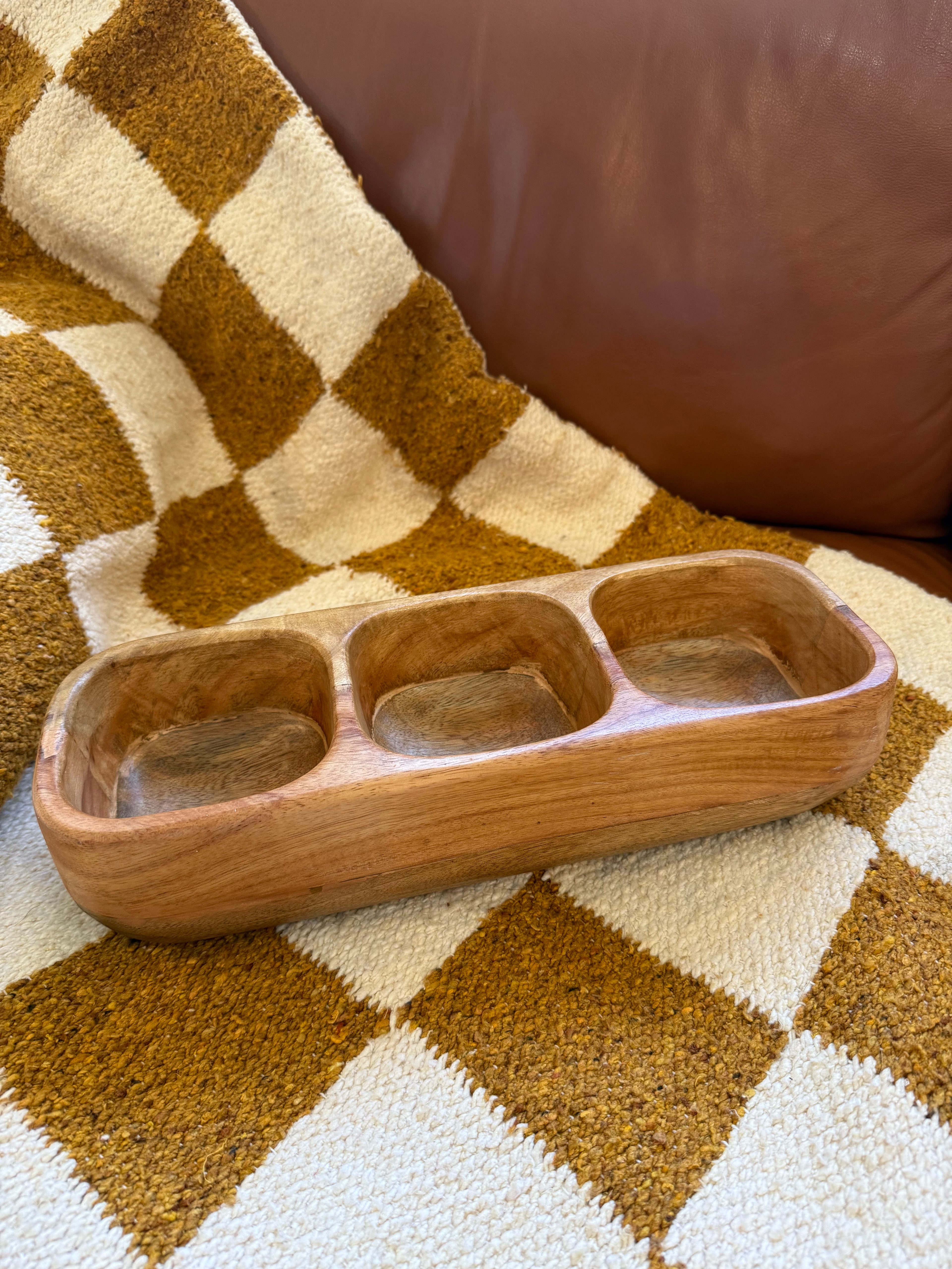 Wooden foot rest on a checkered rug with a brown leather chair.