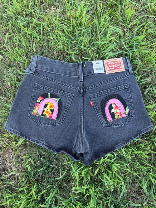 Black denim shorts with embroidered designs on a grassy background