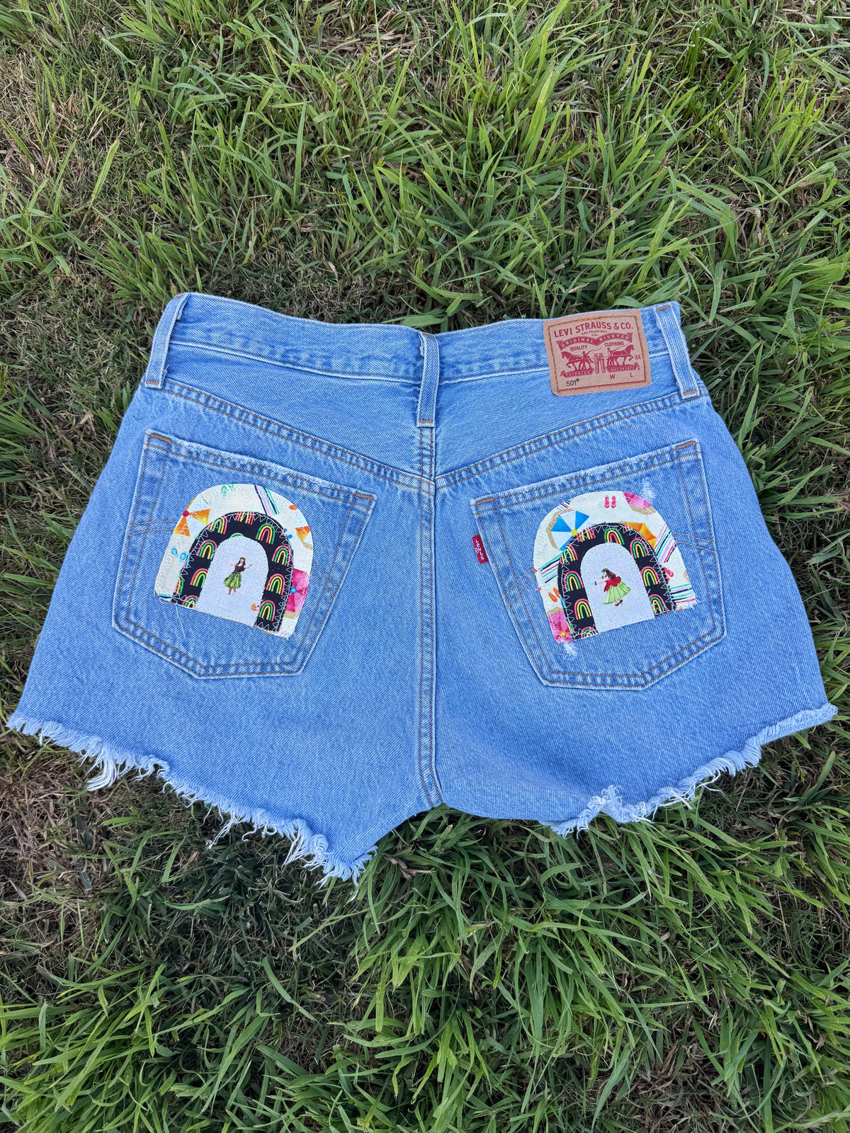 Blue denim shorts with rainbow designs on a grassy background