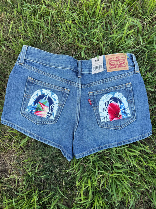 Blue denim shorts with floral designs on the back pockets laid on grass