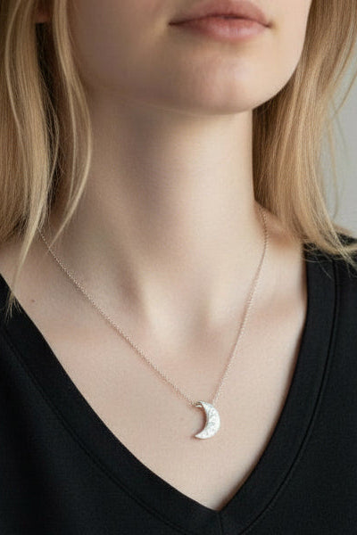 Person wearing a black V-neck shirt with a subtle necklace against a neutral background